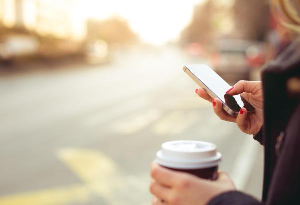 Mujer usando un móvil con un café en la oytra mano